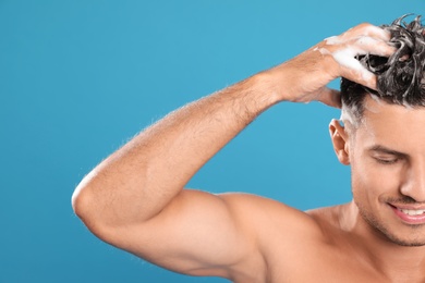 Photo of Handsome man washing hair on light blue background, closeup