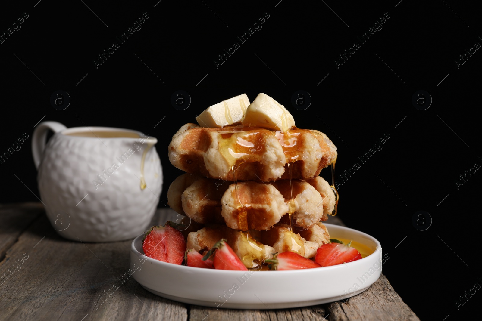 Photo of Delicious Belgian waffles with honey, butter and strawberries on wooden table