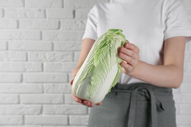 Photo of Woman holding fresh Chinese cabbage near white brick wall, closeup. Space for text