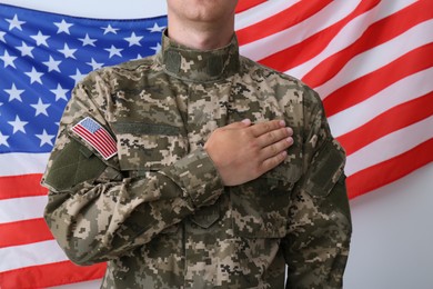 Photo of Soldier holding hand on heart near United states of America flag on white background, closeup