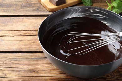 Delicious chocolate cream and whisk in bowl on wooden table, closeup. Space for text