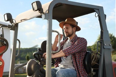 Photo of Farmer in hat driving loader outdoors. Agriculture equipment