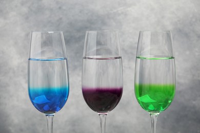 Glasses with liquid and different food coloring on light grey background