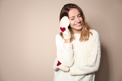 Image of Happy young woman wearing warm sweater and knitted mittens on beige background