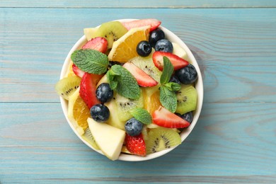Tasty fruit salad in bowl on light blue wooden table, top view