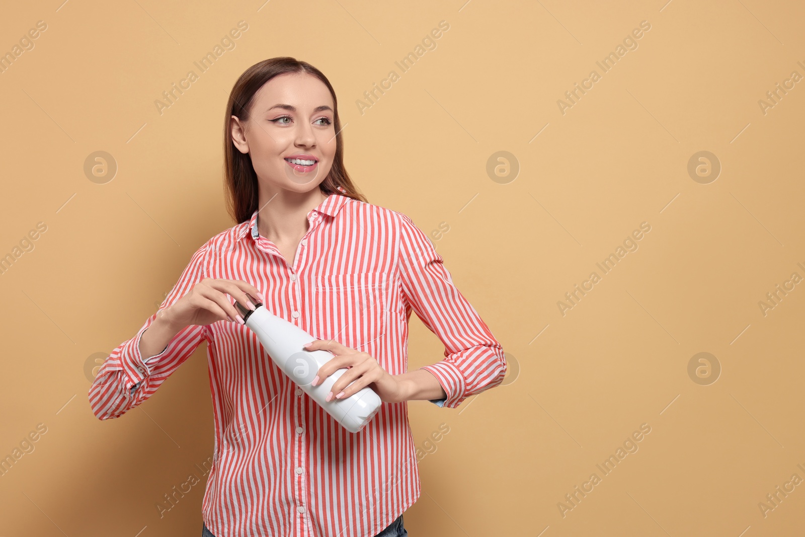 Photo of Beautiful young woman with thermos bottle on beige background, space for text