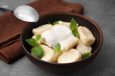 Photo of Bowl of tasty lazy dumplings with sour cream and mint leaves on brown table