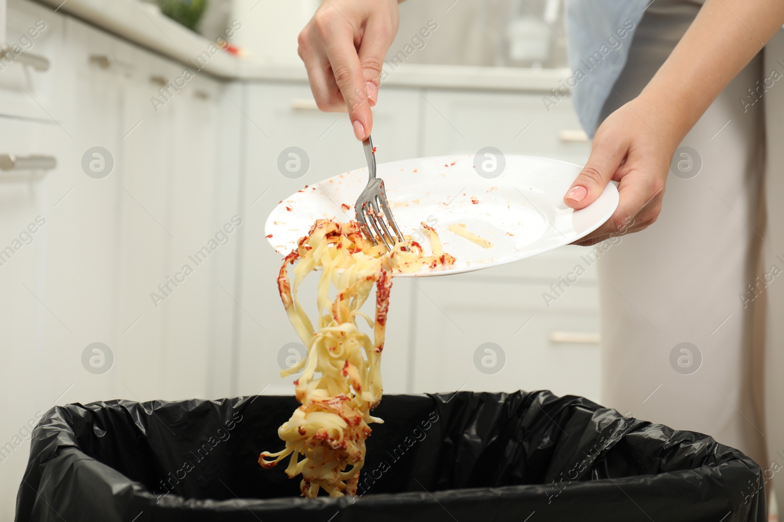 Photo of Woman throwing pasta into bin indoors, closeup