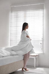 Photo of Beautiful young woman covered with warm blanket near window at home