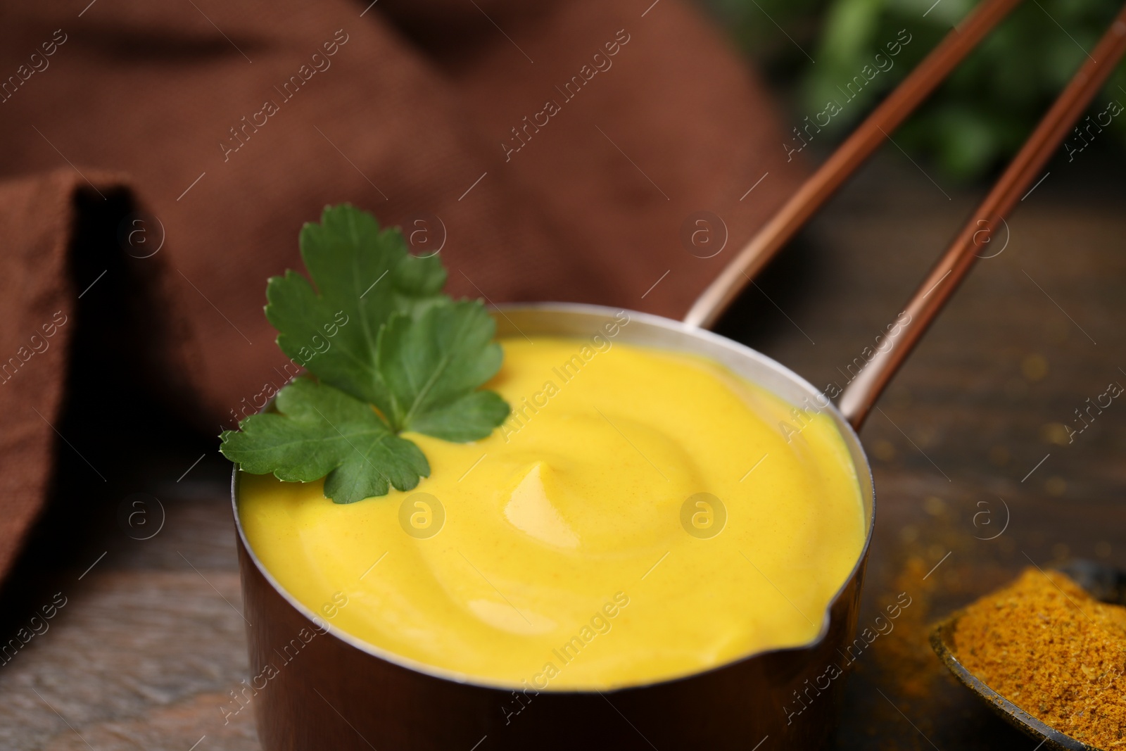 Photo of Saucepan with tasty curry sauce and parsley on table, closeup