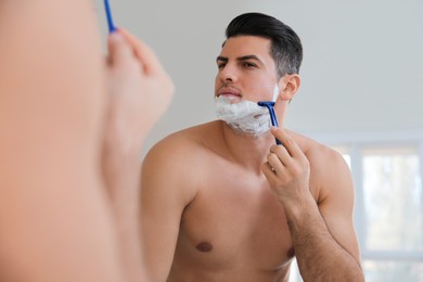 Photo of Handsome man shaving near mirror in bathroom