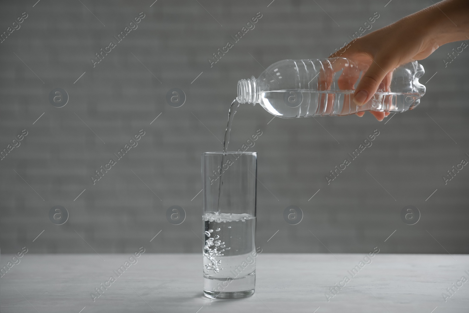 Photo of Woman pouring water from bottle into glass on table against blurred background, closeup