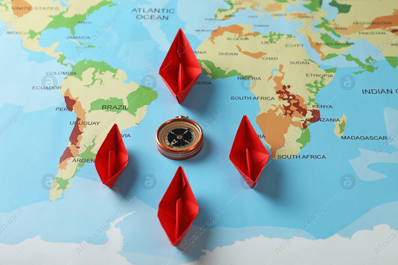 Photo of Bright paper boats and compass on world map, above view