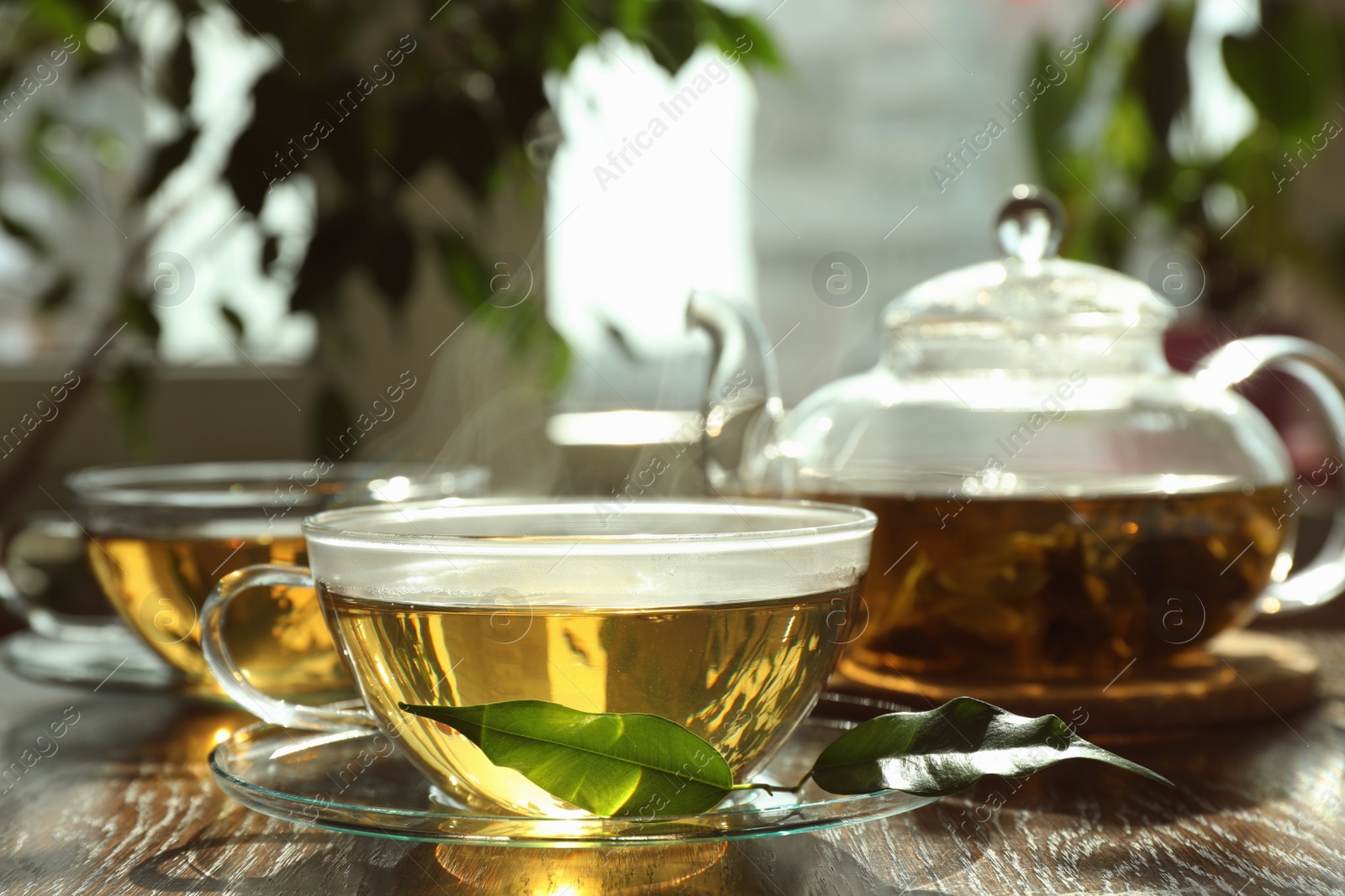 Photo of Fresh green tea in glass cups, leaves and teapot on wooden table