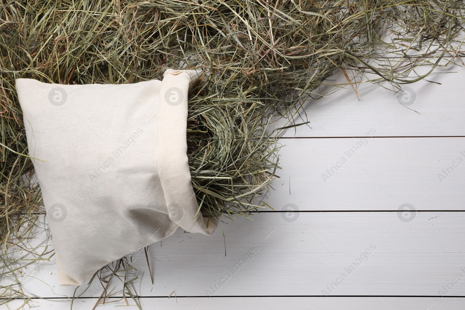 Photo of Burlap sack with dried hay on white wooden table, top view. Space for text