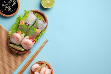 Photo of Delicious spring rolls, shrimps, lime, soy sauce and chopsticks on light blue background, flat lay. Space for text