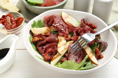 Photo of Delicious bresaola salad with sun-dried tomatoes, pears and balsamic vinegar served on white wooden table, closeup