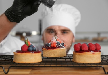 Photo of Male pastry chef sprinkling desserts with sugar powder in kitchen