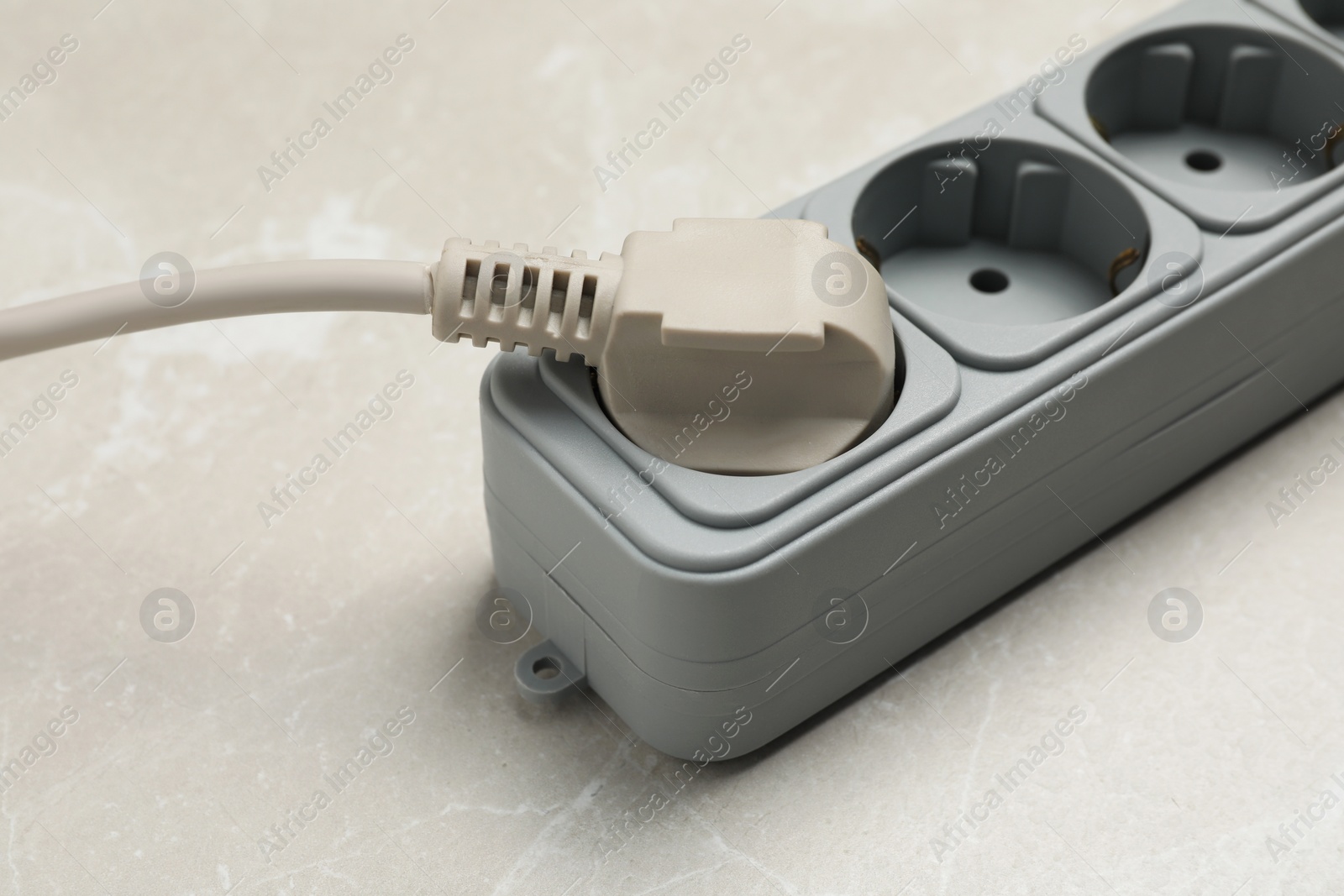 Photo of Power strip with extension cord on grey marble table, closeup. Electrician's equipment