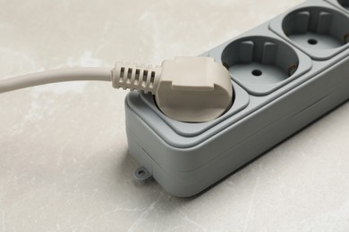 Power strip with extension cord on grey marble table, closeup. Electrician's equipment