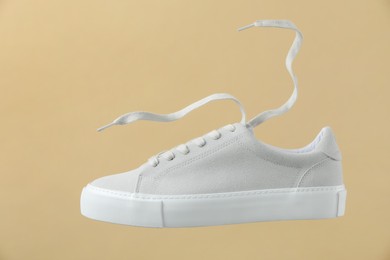 Photo of One stylish white sneaker on beige background