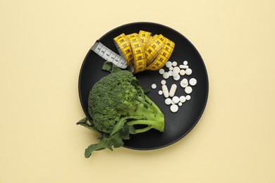 Photo of Plate with weight loss pills, measuring tape and broccoli on beige background, top view