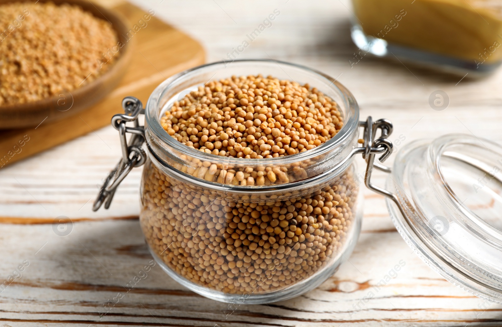 Photo of Mustard seeds in glass jar on white wooden table, closeup