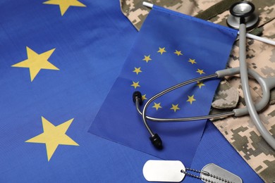 Photo of Stethoscope, tags and military uniform on flag of European Union, closeup