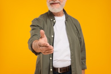 Photo of Man welcoming and offering handshake on yellow background, closeup