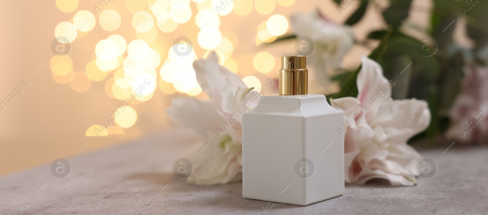 Photo of Bottle of perfume and beautiful lily flowers on table against beige background with blurred lights, closeup. Space for text