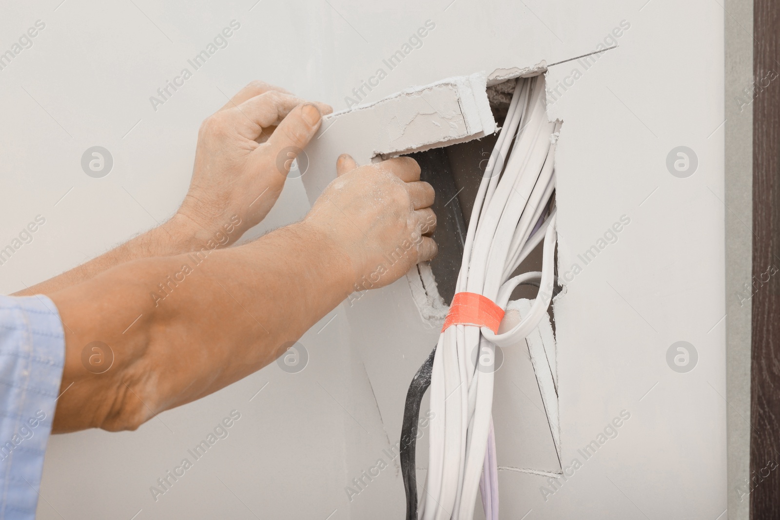 Photo of Electrician preparing place for installing switchboard indoors, closeup