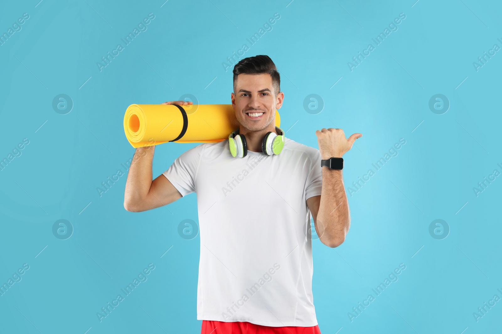 Photo of Handsome man with yoga mat and headphones on turquoise background