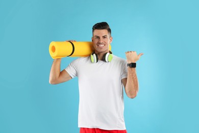 Photo of Handsome man with yoga mat and headphones on turquoise background