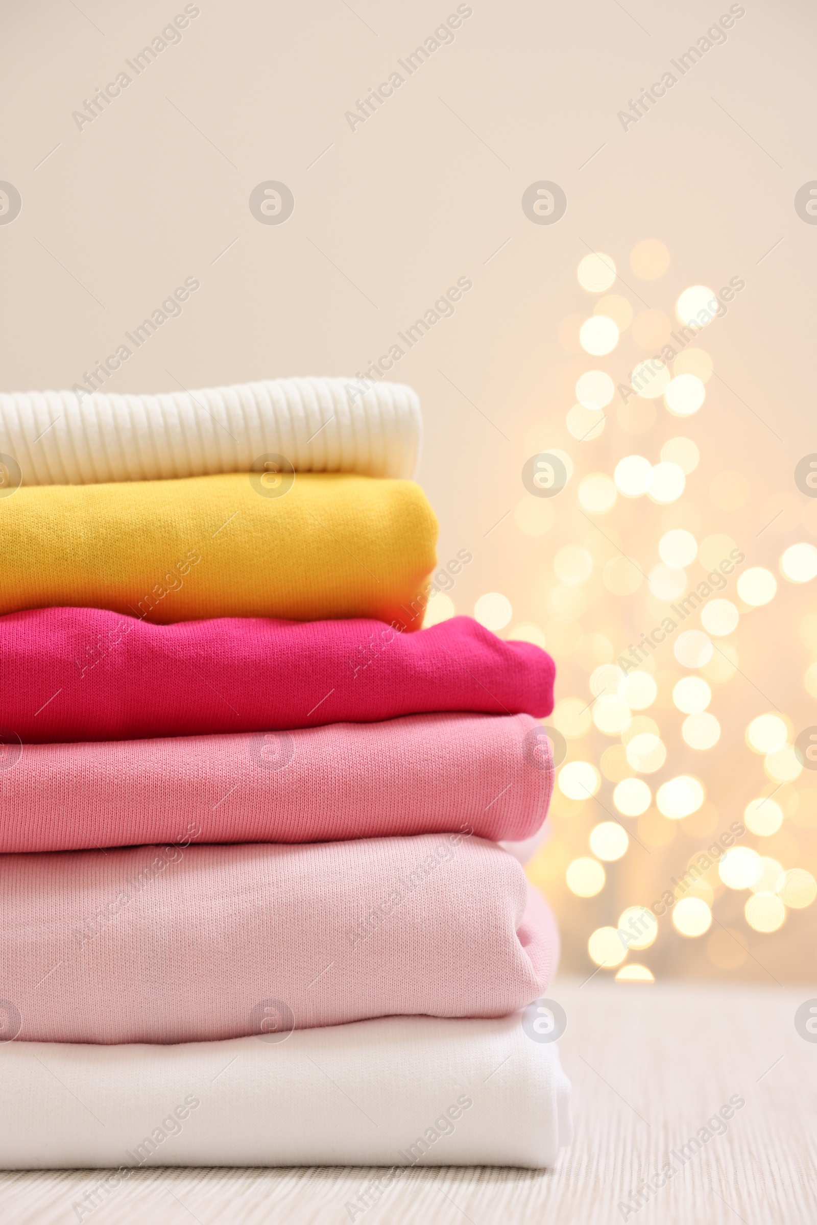 Stack of folded clothes on wooden table against beige background with blurred lights Photo of Stack of folded clothes on wooden table against beige background with blurred lights