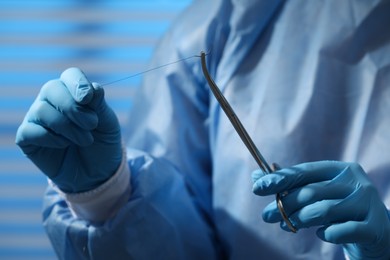 Photo of Professional surgeon holding forceps with suture thread on blurred background, closeup. Medical equipment