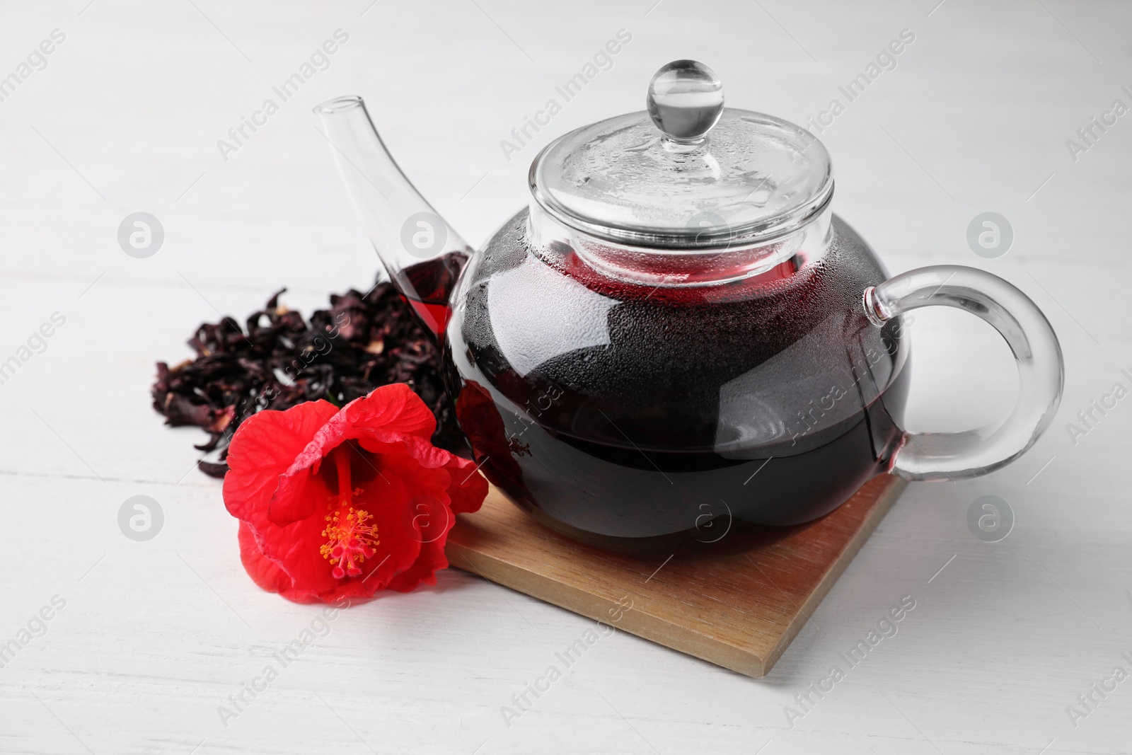 Photo of Freshly brewed hibiscus tea and flower on white wooden table