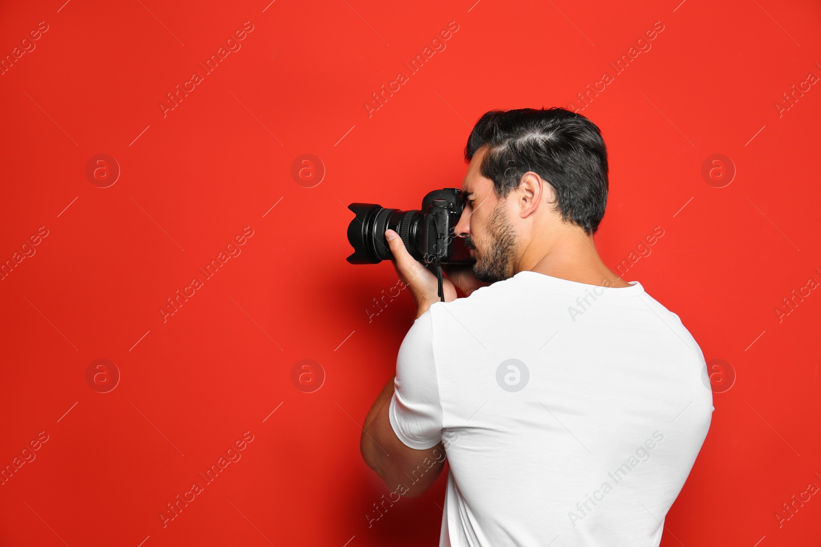 Photo of Young professional photographer taking picture on red background. Space for text