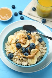 Photo of Tasty oatmeal with banana, blueberries and peanut butter served in bowl on light blue wooden table