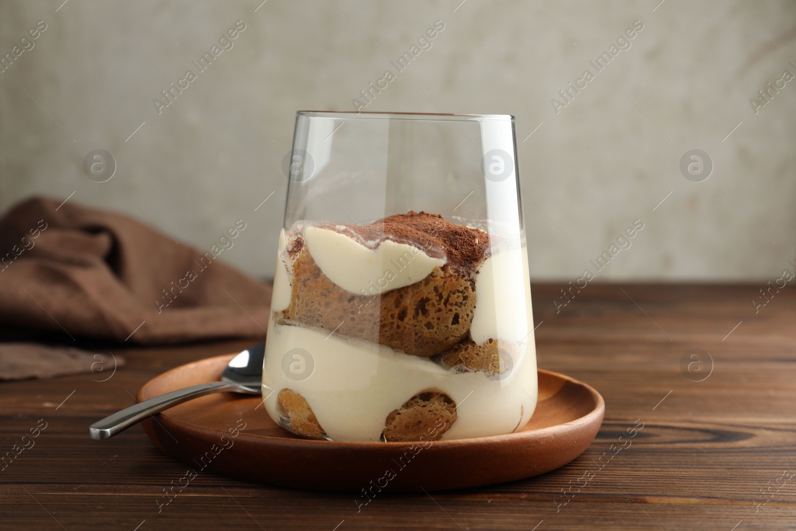 Photo of Delicious tiramisu in glass and spoon on wooden table, closeup