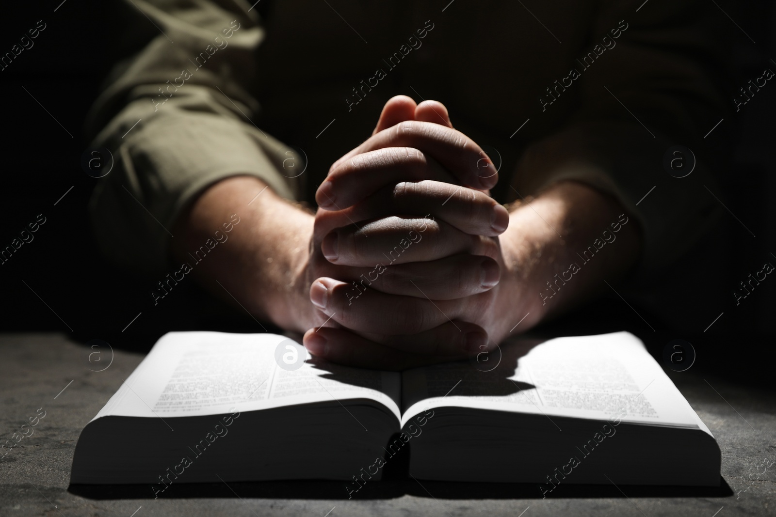 Photo of Religion. Christian man praying over Bible at table, closeup