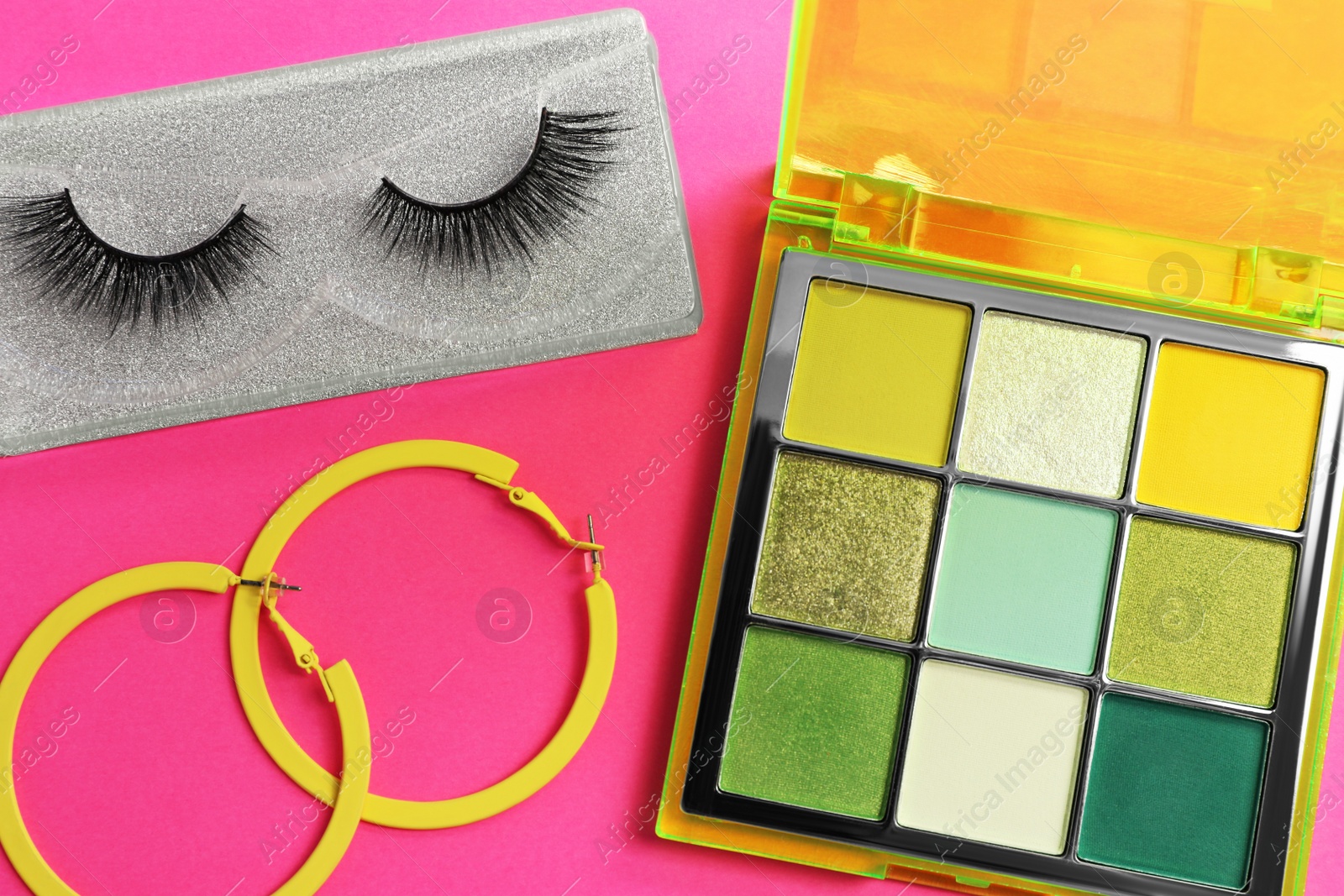 Photo of Colorful eyeshadow palette, false eyelashes and earrings on pink background, flat lay