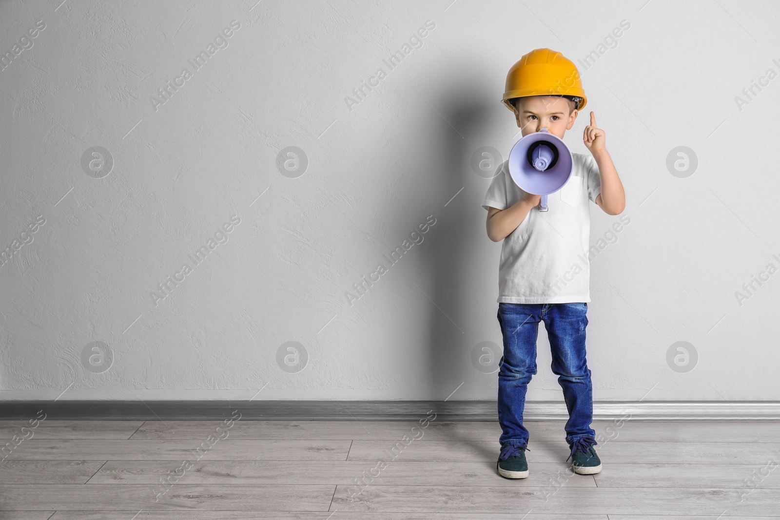 Photo of Adorable little boy in hardhat with megaphone near light wall