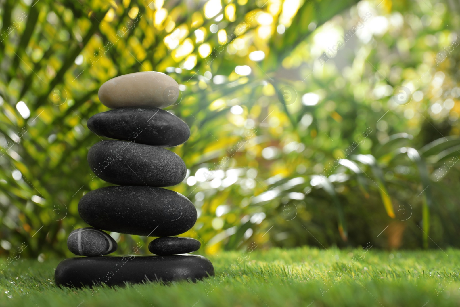 Photo of Stack of stones on green grass against blurred background, space for text. Zen concept