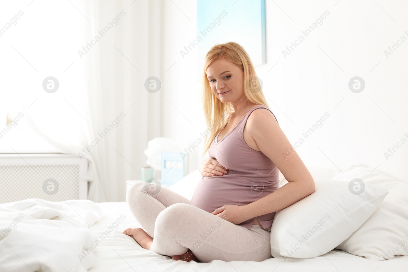 Photo of Pregnant woman sitting on bed in light room