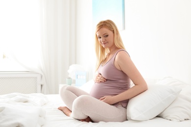 Photo of Pregnant woman sitting on bed in light room