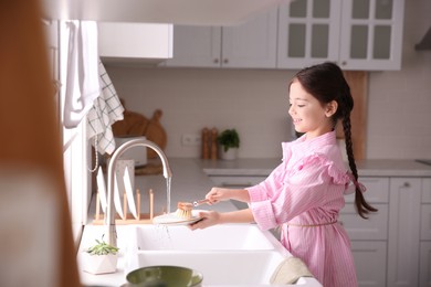 Photo of Little girl washing dishes in kitchen at home