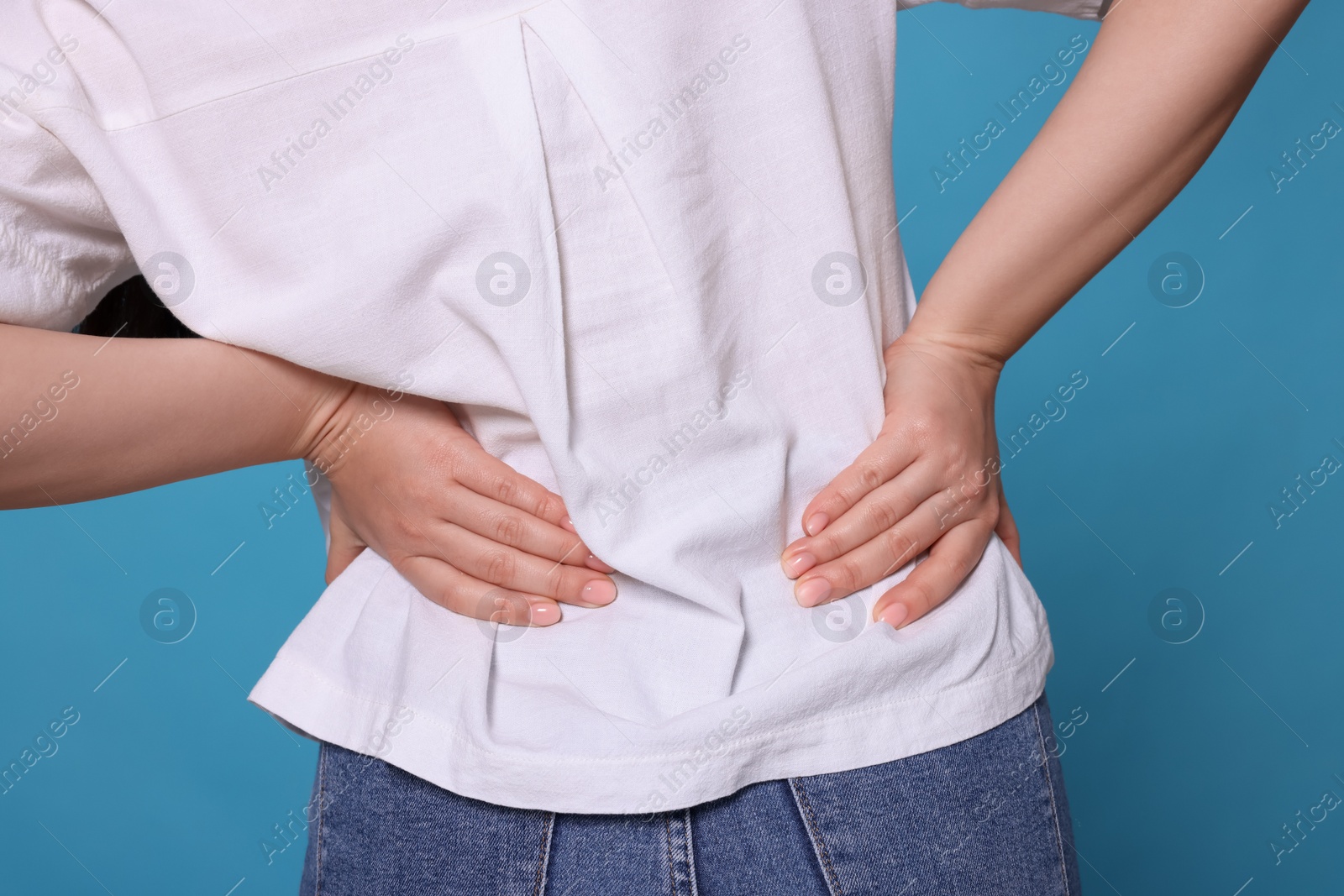 Photo of Young woman suffering from pain in back on light blue background, closeup. Arthritis symptoms