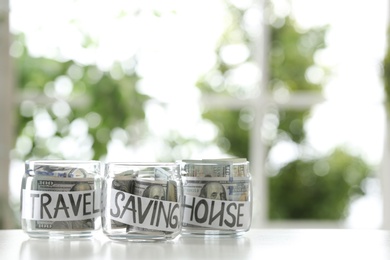 Photo of Glass jars with money for different needs on table against blurred background, space for text