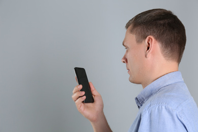 Photo of Man unlocking smartphone with facial scanner on grey background, space for text. Biometric verification