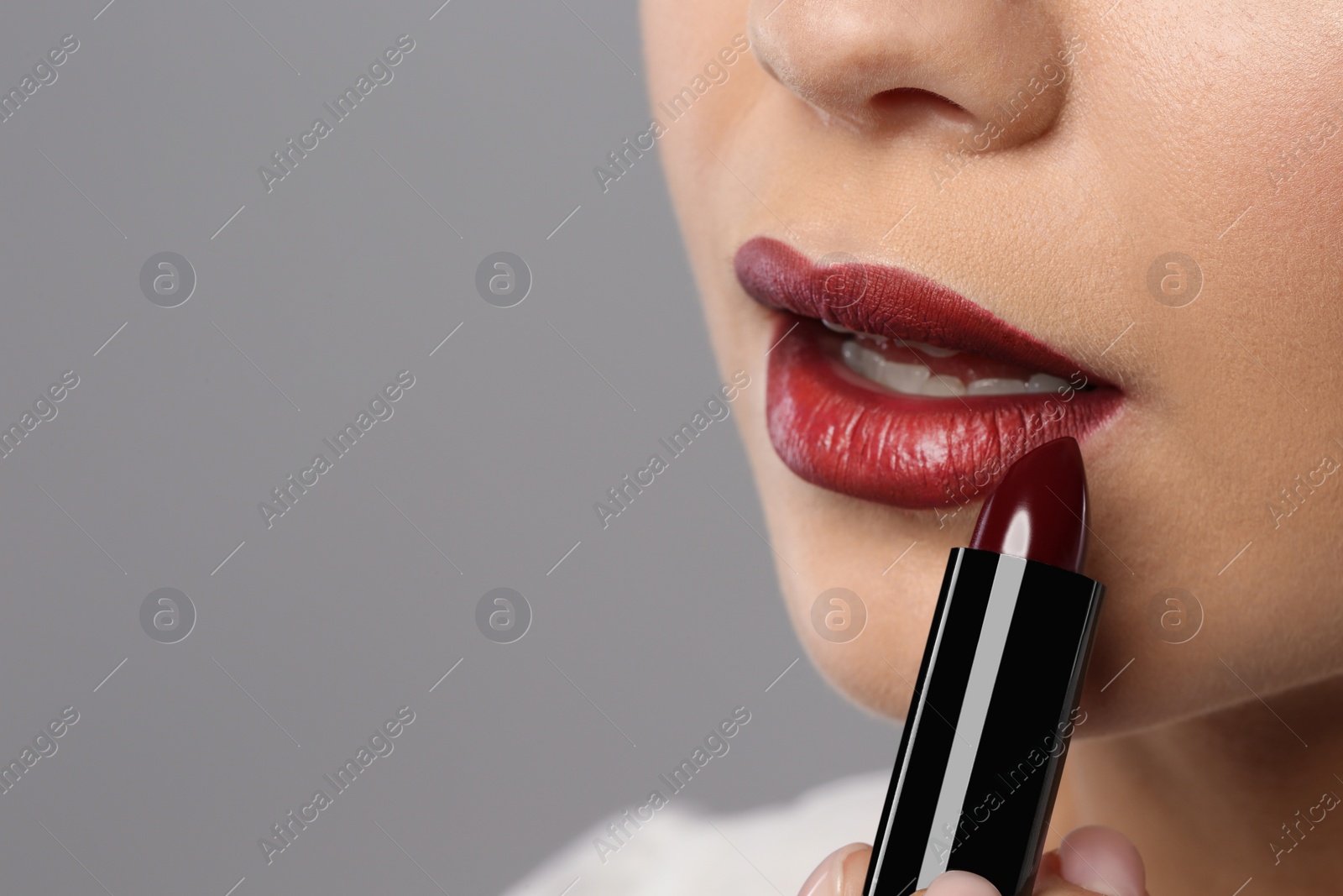 Photo of Beautiful woman applying dark lipstick on gray background, closeup. Space for text